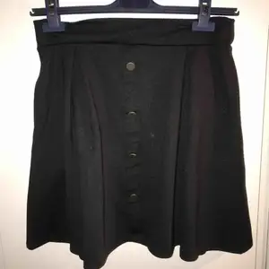 Högmidjad kjol med dekorativa knappar framtill och med fickor! Ganska tjockt material och lite nopprig