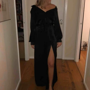  - Elegant svart långklänning med slits från NA-KD, storlek 36.Medföljer ett band att knyta runt midjan. Klänningen knäpps med knappar längs framsidan✨ Aldrig använd🌿 köpt för 600.