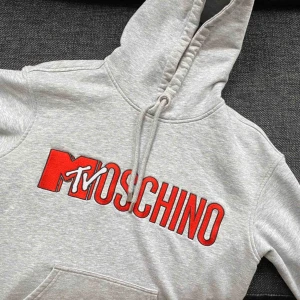 H&M X Moschino Hoodie - Hoodie från Moschino & H&Ms limited edition kollektion, går ej att köpa i butik längre. Fint skick, bara en liten fläck på fickan som knappt syns, kan skicka bild vid intresse. Priser går att diskutera! Högsta budet ligger på 700kr just nu