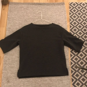  - En grå tröja av lite tjockare, "tvär-räfflat" tyg. Ärmarna  är halv-långa. Man bär den som en varmare  T-tröja. 