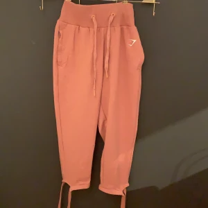 Gymshark byxor - Säljer ett par gymshark mjukis/tränings byxor i storleken S! Färgen är i en typ av stentvättad rosa. Vid benen är de band som man lindrar runt benet för att få en fin detalj. Använt dem 1 gång men säljer dem då de aldrig kommer till användning😊