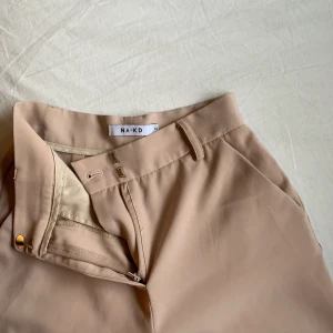 Kostymbyxor - Kostymbyxor från nakd i beige-rosa. Storlek 32, passar på mig som har s/xs och är 176, om man gillar en tightare fit. Byxans modell är ganska korta i benen, och sömmen längs ner är lite frillad, dom kom så nya och det har aldrig stört mig, men värt att notera!✨☀️🌼 skriv privat om du är intresserad!