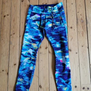 Nike epic lux tights - Nike löpartights i modellen epic lux. Har tre fickor, varav en liten inuti, en stor mobilficka på låret och en stor ficka med dragkedja i svanken. Dragsko i midjan. Medelhög midja. 