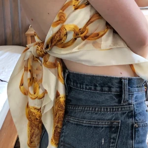 Mönstrad scarf - Vit scarf med ett mönster med guldkedjor, ca 1x1 meter. Köpt på humana men har inte fått nån användning för den. Möts i Stockholm annars betalar köpare frakt. 