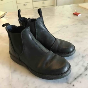  - Boots i äkta läder. Skaft med resår i vardera sida. Rundad tå. Tillverkad av äkta läder. Insida av äkta läder och textil. Yttersula av gummi Storlek 37