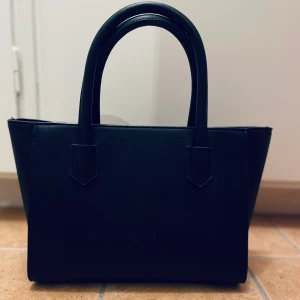 Svart väska från Zalando - Oanvänd väska från Zalando, har lyckats spilla en kräm på den som tyvärr inte går bort.. prissänkt pga det. Frakten ingår inte i priset!  Nypris: 200