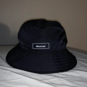 Monclear hatt storlek L - Väldigt fin monclear bucket hat köpt på nk för några månader sedan, inga fläckar eller annat. Inte andvönd så mycket. Nypris 1900kr.                       frakt ingår i priset