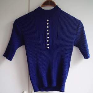 Marinblå stretchig tröja från 70- eller 80-tal. Finns ingen lapp men är förmodligen inte heller hemmasydd. I fint skick och med fina vita dekoknappar.