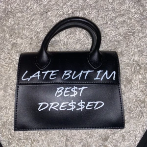 Svart väska - Boohoo - En helt oanvänd svart väska med text där det står ”late but im best dressed” från boohoo. En guldig kedja till. Aldrig kommit till användning men jättefin. 