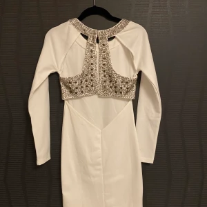 Festklänning med glittrig rygg - Fin festklänning som passar perfekt till nyår! Vit med läcker rygg försedd med pärlor. Framhäver figuren på ett snyggt sätt.  Använd endast ett fåtal gånger.  Kvalitet: 68% viskos, 27% polyester, 5% elastane