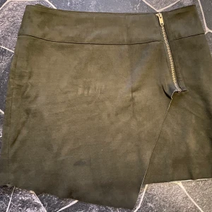 Kjol - Mörkgrön kjol i mockatyg, använd 1 gång. Man drar igenom en knapp på insidan men när den köptes var hålet nästan för stort för knappen enligt mig. Går ju att byta till större knapp, men funkar även som den är nu. Fint skick! 
