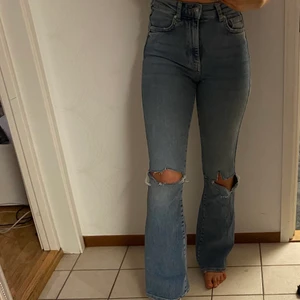 Jeans med hål - Utsvängda jeans med hål i knäna. Köpta från Gina Tricot. Använda några gånger, jättesköna och stretchiga. Strl 34.