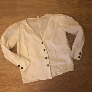 Blus från H&M trend - Vit bomullsblus/skjorta från HM trend, mörkbruna knappar fram och på ärm. Fint skick!