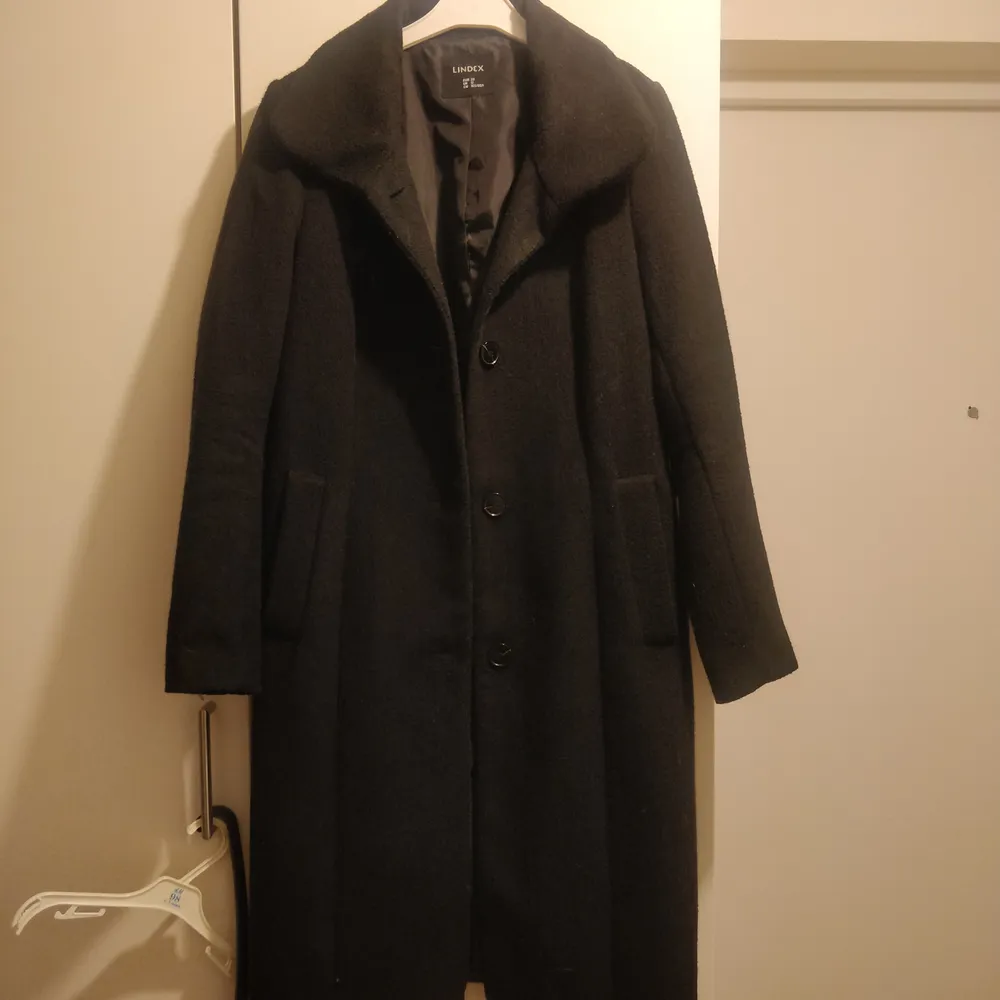 En svart ullkappa med skärp från Lindex i storlek 38. Köpt för 800 kr. 85% polyester, 15% ull. Jackor.