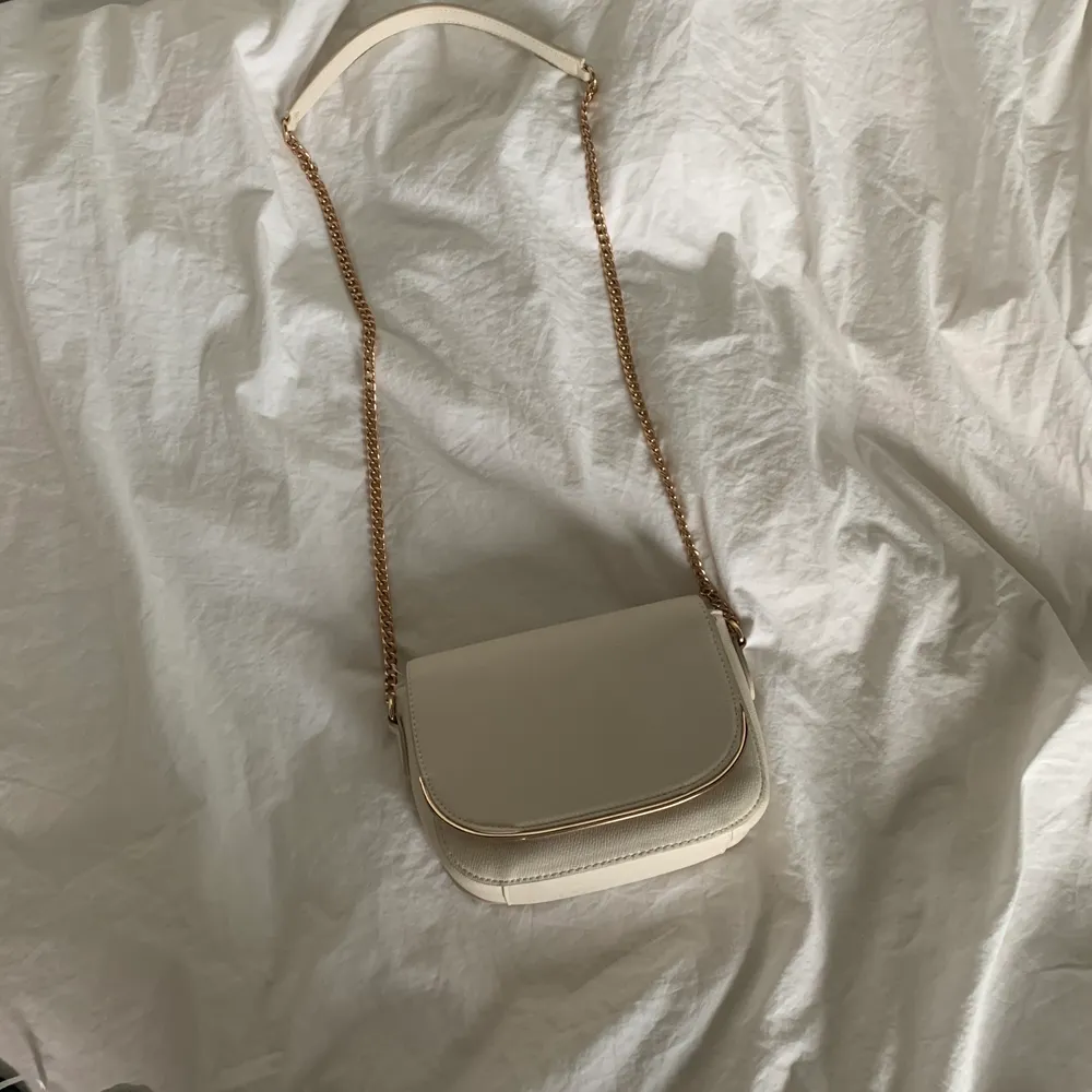 Säljer min väska från HM! Väskan har andvänds fåtal gånger men är i toppskick. Väskan är beige med guldiga detaljer. Väskan finns ej kvar i butik. Kjedjan är 40cm lång på vardera sida (40x2). Är ca 165cm lång och väskan går ner till höften. Vid mer frågor och intresse kan du meddela mig på appen. Pris:120kr +frakt . Väskor.