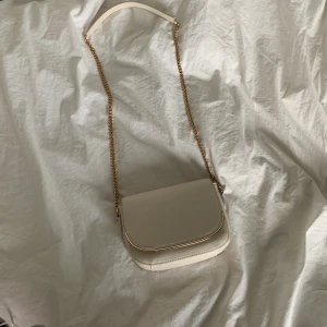 🛑Handväska från HM!🛑 - Säljer min väska från HM! Väskan har andvänds fåtal gånger men är i toppskick. Väskan är beige med guldiga detaljer. Väskan finns ej kvar i butik. Kjedjan är 40cm lång på vardera sida (40x2). Är ca 165cm lång och väskan går ner till höften. Vid mer frågor och intresse kan du meddela mig på appen. Pris:120kr +frakt 