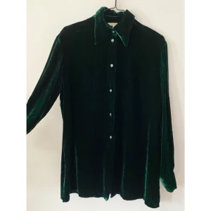 Grön sammetsskjorta, M - Grön sammetsskjorta från Ebba Jensen i stl M. Av viskos och siden. Bra skick förutom ett litet hål fram på vänster sida (se bild 3). Kan postas mot 55kr porto.