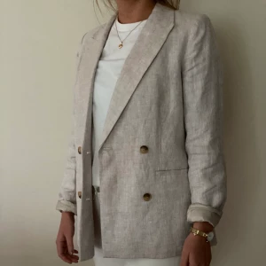 Kavaj - Beige linnekavaj i stl 34, dock stor i storleken så mer som en 36. Slits i mitten baktill. Rak modell. Dubbla knappar framtill i brunt. Märke Wera från Åhléns.