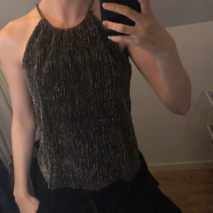 Guldglitter topp - En svart- guldglitterig topp med knytte där bak från H&M endast använd en gång i prima skick. 