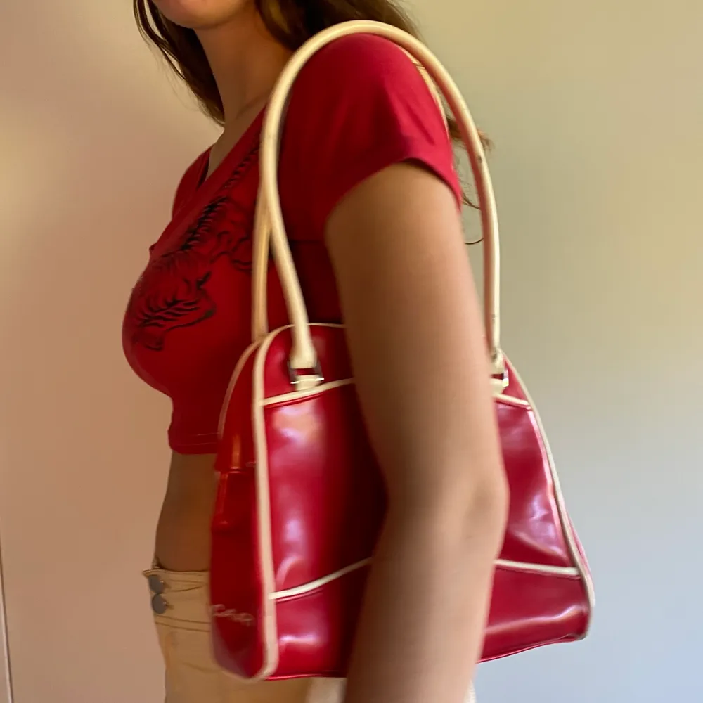 Röd väska i retro-stil. Den är glansig med metallförslutelse som man knäpper ihop. Lite sliten men fortafarande fräsch. Säljer på grund av att den inte passar min stil längre. Frakt 63kr. Väskor.