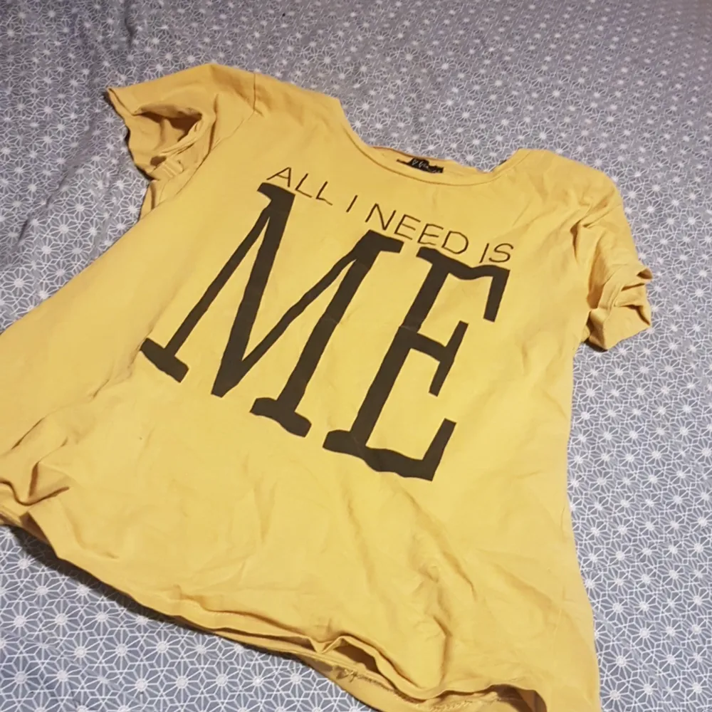 Det är en gul t-shirt med en liten text där det står ALL I NEED I ME. Köparen betalar frakt.. T-shirts.