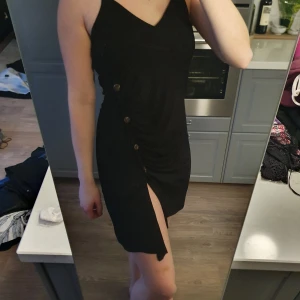 Klänning från Nelly med slits - Svart klänning från Nelly trend med knappar och slits. Som ny då jag använt den fåtal gånger. Storlek XS men funkar på mig som vanligtvis är S.