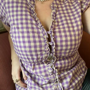 Söt vit och lila rutig blus - Vit och lila rutig blus som går in i midjan och har knappar fram till💜 Den är i secondhand skickt! Personen på bilderna bär oftast medium och är 173 cm lång. Köparen står för frakt! 