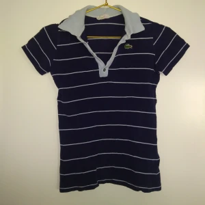  - Randig piké i blått från Lacoste.  Skick: Begagnad.  Gratis frakt!