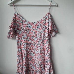  - BLOMMIG KLÄNNING FRÅN URBAN OUTFITTERS LONDON. Aldrig använd, endast varit nerpackad i en klädlåda. Säljer pga för liten storlek för mig. Off the shoulder klänning. Ordinarie pris 500 kr. Köparen står för frakten. 