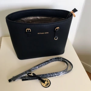Michael Kors Väska - Helt ny Michael Kors väska🍀inte ens provanvänd, ligger i skyddspåse, tillbehören är fortfarande inplastade. Perfekt storlek till dator/böcker/skrivblock. Hårt material, håller formen. Skriv gärna för frågor/fler bilder😊 Hittar tyvärr inget äkthetsintyg därav priset. Möts helst upp för frakt kmr bli väldigt dyrt för dig annars. Pris kan diskuteras vid snabb affär