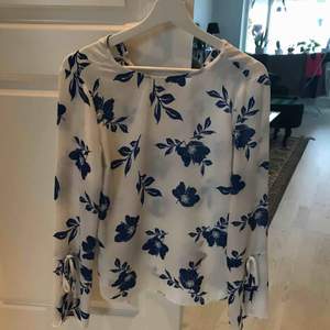 Blus med blommigt mönster. Knäppe i nacken och delvis öppna armar med knyten. 80 kr + frakt 39 kr