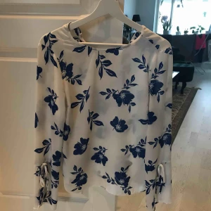  - Blus med blommigt mönster. Knäppe i nacken och delvis öppna armar med knyten. 80 kr + frakt 39 kr