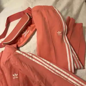 Träningsbyxor från Adidas i färgen peach/gammelrosa. Finns helt set med jacka och crossbodybag/magväska. Köp hela setet för 700 kr