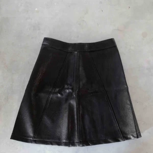  - Svart kjol i läderimitation med dragkedja på baksidan.