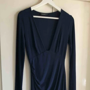  - Blå/marinblå asymmetrisk klänning från Nelly. Djup urringning. Långärmad. Stretchig material. Köparen står för frakten. 