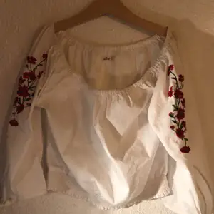 En off-shoulder tröja med rosor sydda på armen. Den har knytningar längst ner på ärmen (skicka om du vill ha bilder:) 