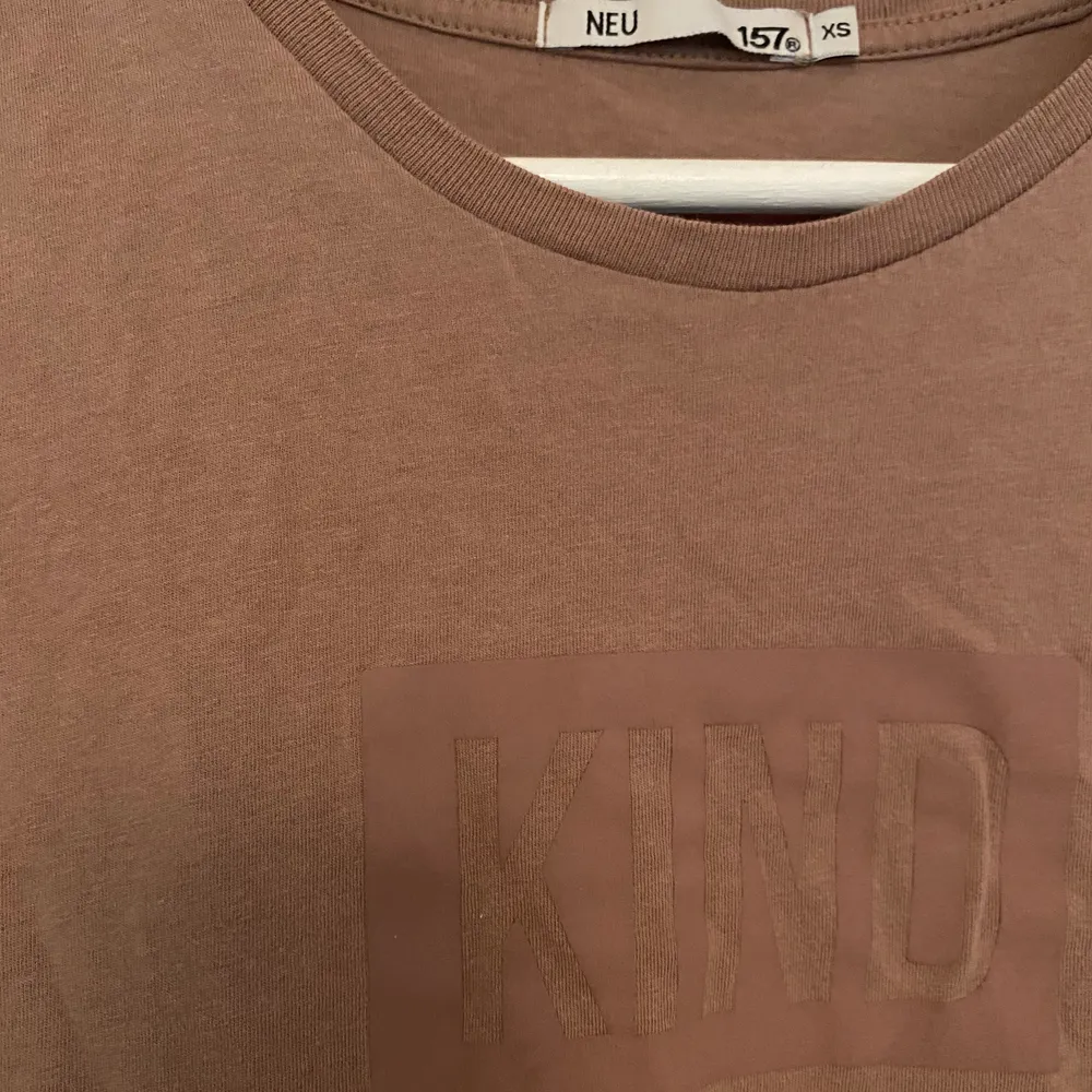 Beige t-shirt. Tryck:”kind”. Köparen står för frakt. T-shirts.