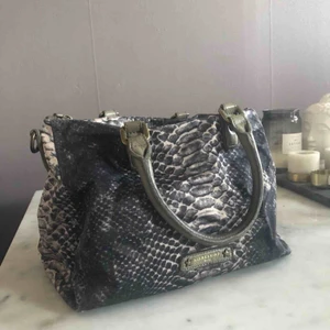  - Ingår dust bag!  - I orm imitation på utsidan - Innehåller 4 fickor varav en stor med dragkedja. - - -Flitigt använd.  -Inga defekter!  -Väskan är 30cm lång, 22cm bred och likaså djupet från botten till dragkedjan