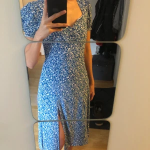 Blommig Klänning - Superfin klänning med sidoslits och dragkedja i ryggen. Jag är 157 cm och klänningen är i min knä längd. Bara använd en gång i somras! Först till kvarn!