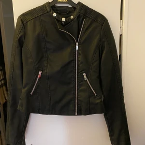  Bikerjacka från Nelly stl S - Jättesnygg svart bikerjacka i konstmaterial från Nelly i stl S. Snygga dragkedjor längst ner vid ärmarna samt snygg sned dragkedja fram. Fint skick. 