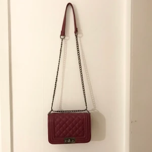 Axelremsväska vinröd - Vinröd/burgundy axelremsväska köpt på Gina Tricot. Använd ett fåtal gånger har dock någon form av små färgskador på kedjan men detta syns ej längre ifrån. Finns ett litet fack i väskan som är bra för kort eller liknande. Köparen betalar frakten. :)