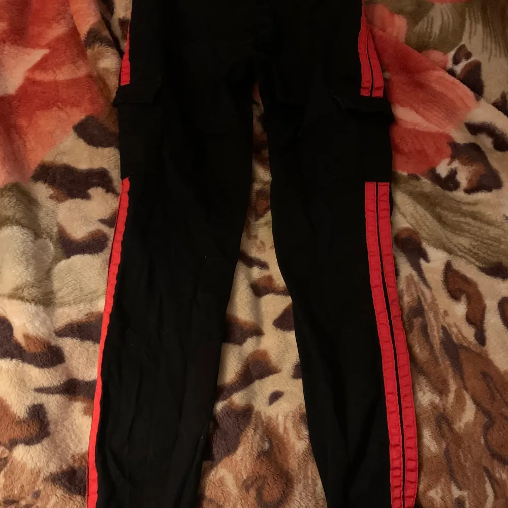 Svarta byxor med röda sträck på sidorna. Har 2 fickor fram och 2 fickor på sidorna. Jeans liknande material. Storlek S. Jeans & Byxor.