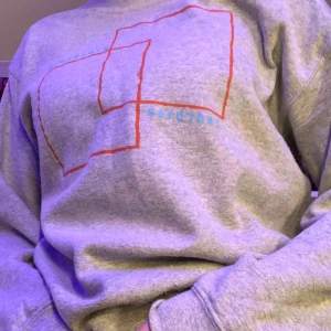  - Grå sweatshirt med motiv. Bra skick. Motivet föreställer röda fyrkanter och en turkos text. 