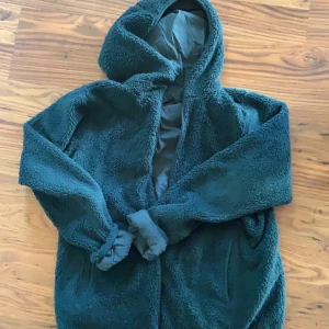 Vändbar teddyjacka/vindjacka/mellanlager - Mörkgrön, vändbar jacka med supermjuk teddyfleece på ena sidan och prassligt vindjackematerial på andra sidor. Finns fickor på båda sidor. Strl L herr, men kan bäras som oversize. Pris kan diskuteras!