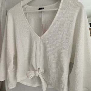 Vit topp med knytning - Aldrig använd, vida ärmar, lite kortare i midjan och knytning fram. 