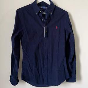 Oanvänd Ralph Lauren skjorta i mocka, färgen marinblå med ett rött märke. Kan mötas upp i Göteborgs trakterna annars betalar köparen för frakten.