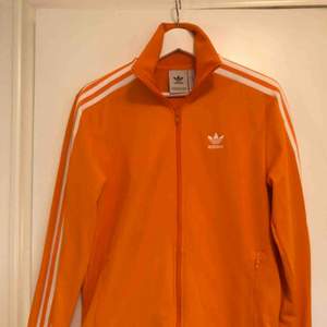 Fräsch orange Adidas tracksuit-top i nyskick!!! Använd 1 gång! Kan mötas upp, alternativt posta, frakt ligger dock på köparen. Swish
