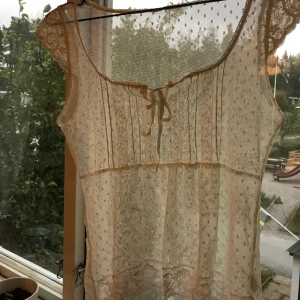 Vit spetstopp i nät - Gräddvit genomskinlig topp i nät av spets med knytning fram och mycket olika detaljer. Storleken skulle jag säga är 36.