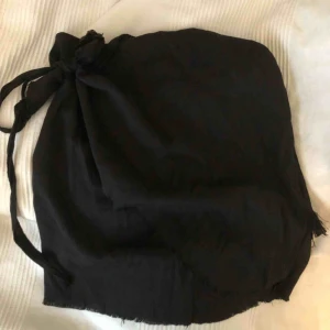  - En jättefin svart kjol i tyg som man knyter runt midjan, den har en dragkedja på sidan och är lite halft fransig nere på kanten, använd några gånger men i bra skick, den är i medium men passar även mig som har S