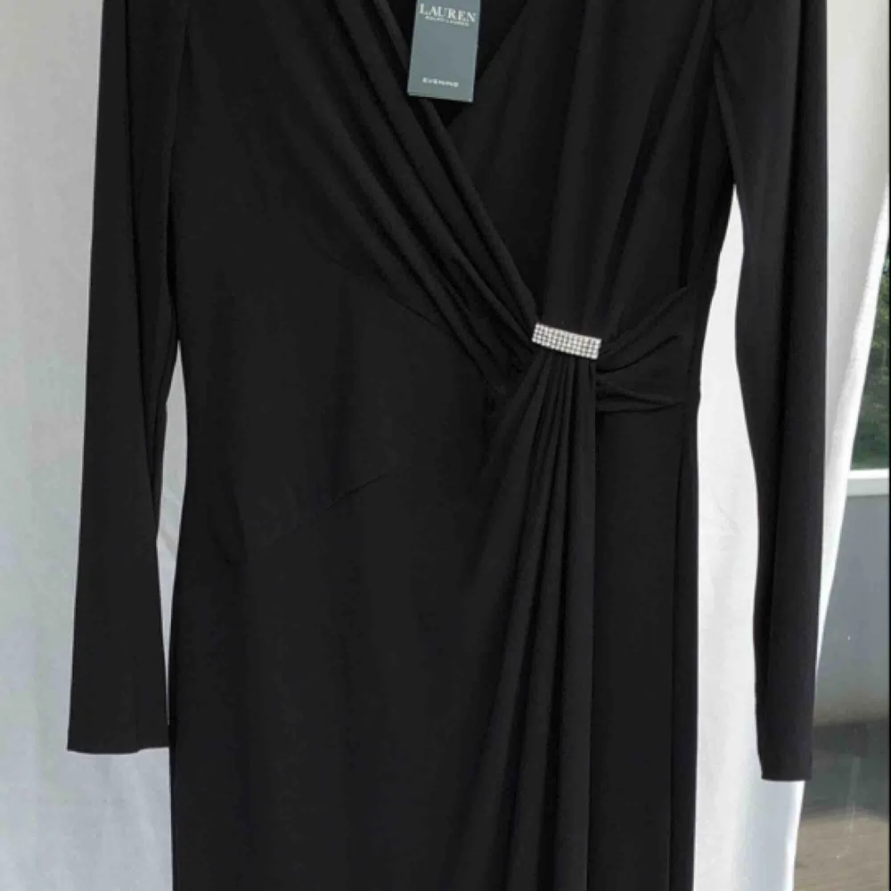 Vacker, oanvänd hellång svart klänning från Ralph Lauren! Köpt i början av sommaren, men tillfälle gavs aldrig att använda den. Strl 42 men är aningen mindre i strl! Glittrigt spänne i sidan, omlottmodell över bysten. Stilfull slits på vä sida. . Klänningar.